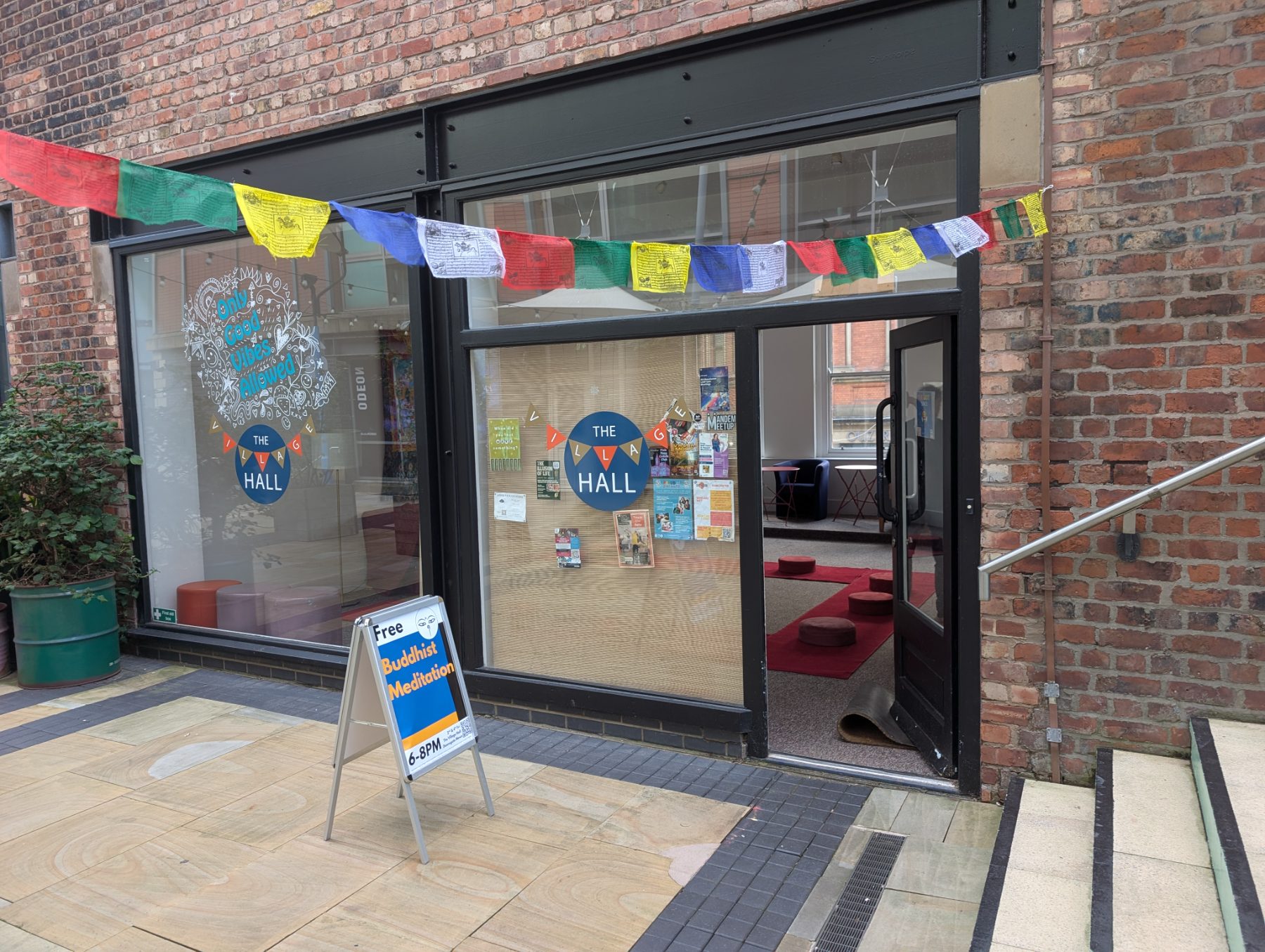 The Village Hall entrance on Deansgate Mews, with prayer flags and a Free Buddhist Meditation sign